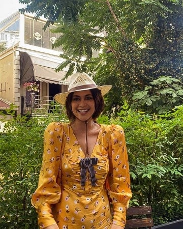 Yasmine Al Massri looks gorgeous in her yellow dress and white hat with green natural background.